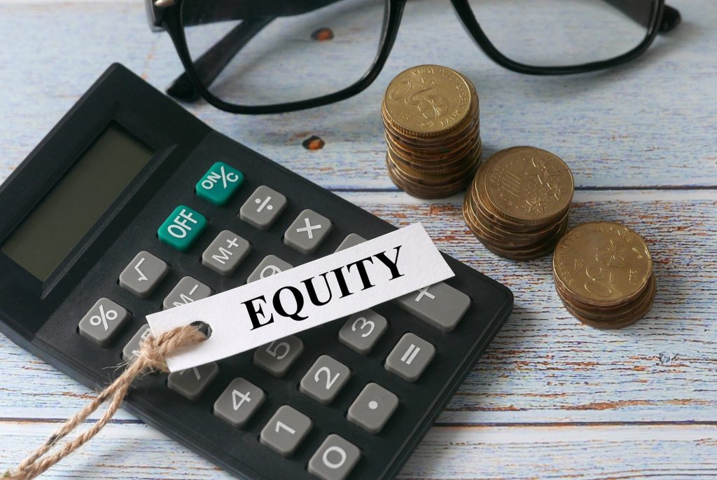 Calculator,glasses,stack of gold coins and paper tag written with word Equity on wooden background.